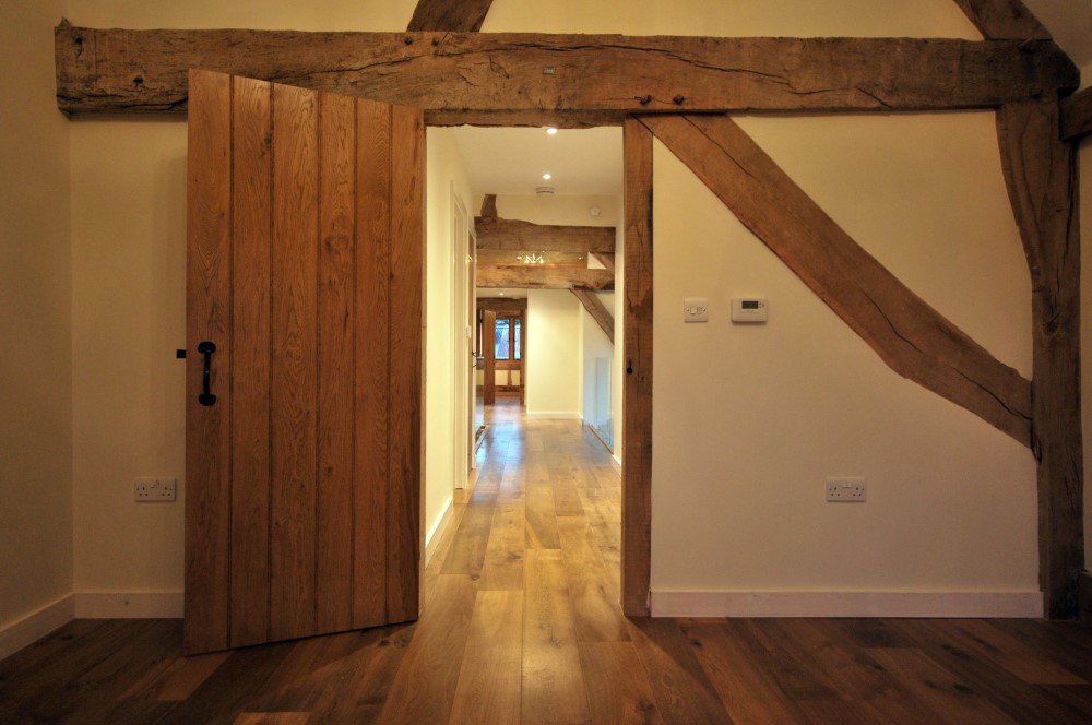 Barn conversion view through wooden doorway with exposed timber and beams Surrey - Vernacular Homes
