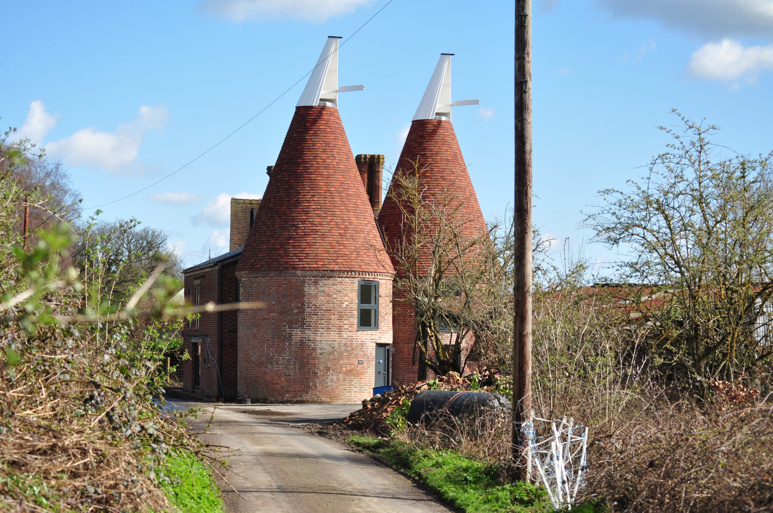 Driveway up to converted oast with two new kiln roofs topped with white cowls, new contemporary grey blue front door and glazing.